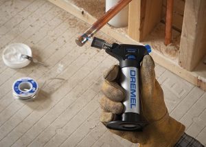 Gloved hand holding butane torch in home workshop